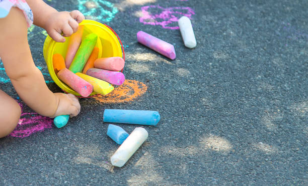 The child draws with chalk on the asphalt. Selective focus.