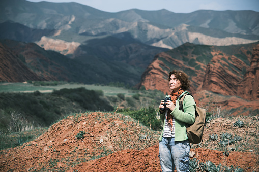Female backpacker is looking at binocular at red rocks and remote mountains