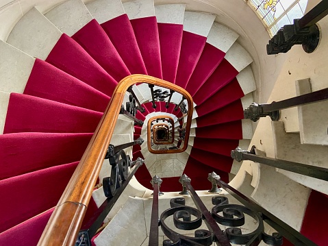 Looking down on a stone spiral staircase lined with a red carpet in an old apartment building in Paris, France