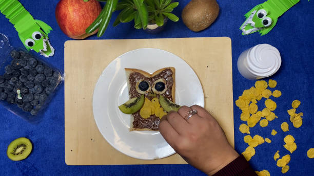 istock Creative kids meals. female hand putting cornflakes on chocolate spread making it in owl shape for kids 1486547966