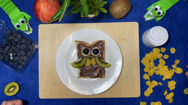 istock Creative kids meals. female hand putting cornflakes on chocolate spread making it in owl shape for kids 1486548749