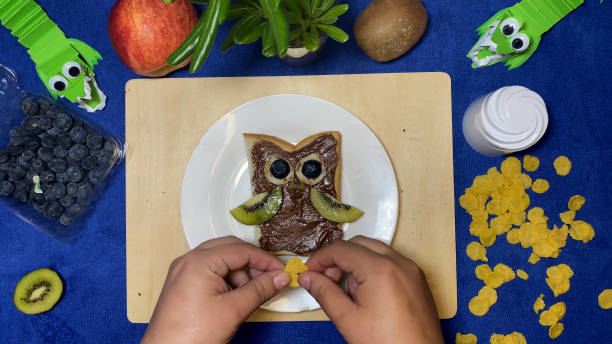 istock Creative kids meals. female hand putting cornflakes on chocolate spread making it in owl shape for kids 1486548880