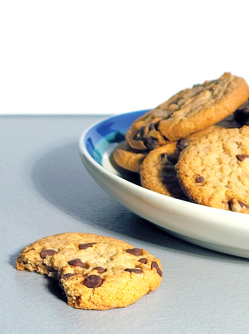 Plate of Chocolate Chip Cookies - one with a bite out of it in the foreground - gray table with white background