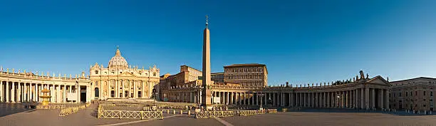 Panoramic blue summer skies over Michelangelo's golden facade of St. Peter's Basilica, the Vatican apartments and museums, Bernini's monumental colonnade and the obelisk in Piazza San Pietro, Vatican CIty, Rome, Italy. ProPhoto RGB profile for maximum color fidelity and gamut.