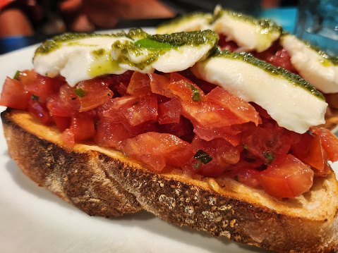 Bruschetta is an Italian antipasto made with bread and grilled with olive oil, cheese, sliced tomatoes and basil.