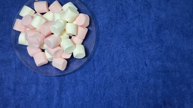 White and pink marshmallows in the transparent plate spinning over the blue surface. stop motion