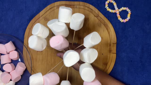 Marshmalows on the sticks. Female hand colecting marshmallows like bouquet of flowers over the wooden board