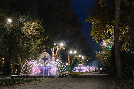 Khujand, Tajikistan. October 16, 2019: Park Kamal Khudzhandi alee with  with beautiful evening illumnation ,musical fountains and motion blurred people.