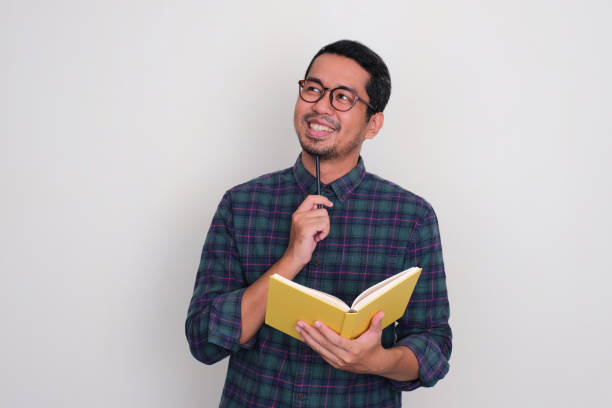 istock Adult Asian man thinking about something while holding a book and pen 1486565514