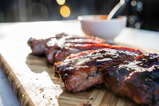 A mouth-watering rack of barbecue pork spare ribs, sliced and ready to serve, sits on a rustic wooden cutting board, tempting taste buds at a lively backyard barbecue.