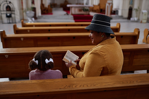 African American grandmother reading Bible to her granddaughter in church, she teaching christian customs to her