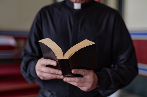 Close-up of priest reading Bible book during ceremony standing near the altar in church