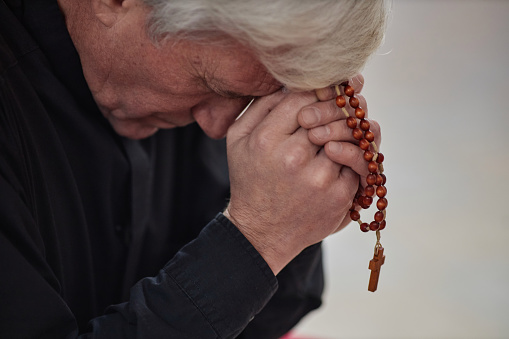 Close-up of senior man with grey hair praying with rosary beads in his hands