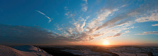 Beautiful orange light illuminating sparkling snow covered ridges looking out over the white valley vista of patchwork Herefordshire Welsh Marches farmland and rolling Malvern Hills under panoramic skies. ProPhoto RGB profile for maximum color fidelity and gamut.