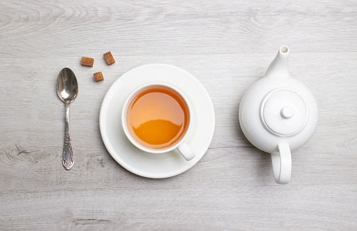 Cup of Tea and teapot, spoon, sugar, on a light wooden background