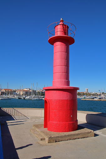 The photo was taken in the coastal Spanish city of Cambrils. The picture shows a bright red lighthouse at the entrance to the city's marina.