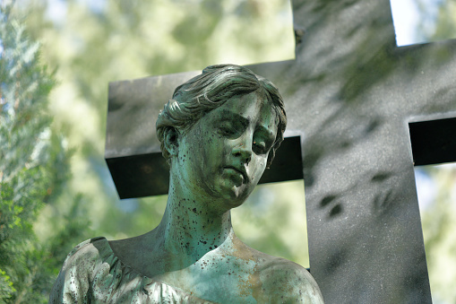 Old copper angel statue and a stone cross in a cemetery