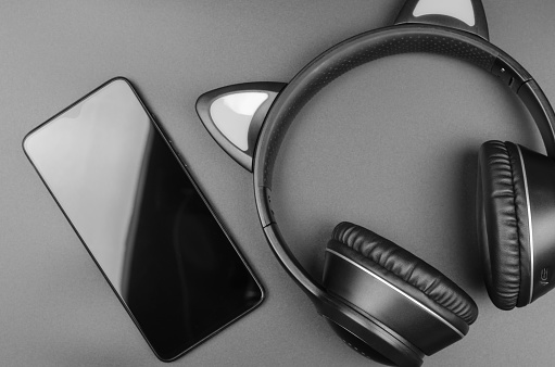Wireless headphones and smartphone on black background, selective focus