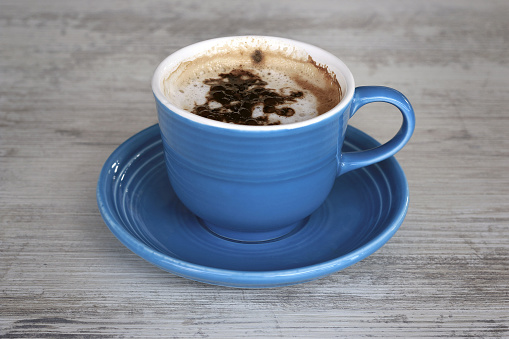A blue cappuccino cup on a grey wooden table.