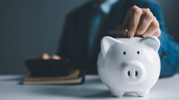 istock Saving money concept. Building a Solid Financial Future: Unlocking the Secrets of Savings, Investments, and Wealth Creation. Businessman put coins into white piggy bank, planning to retirement. 1486581398