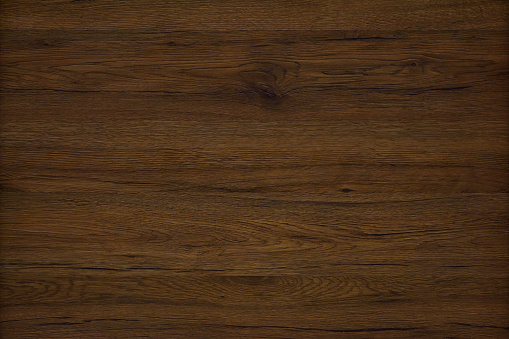 Dark brown wood background. Wood texture, cracks and knots are strongly expressed. A wood grain pattern featuring even grains of wood running vertically across the image.