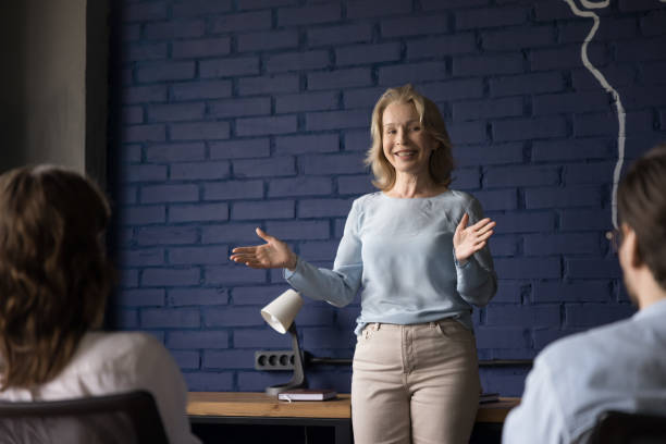 istock Friendly positive senior corporate teacher woman speaking before group 1486590953