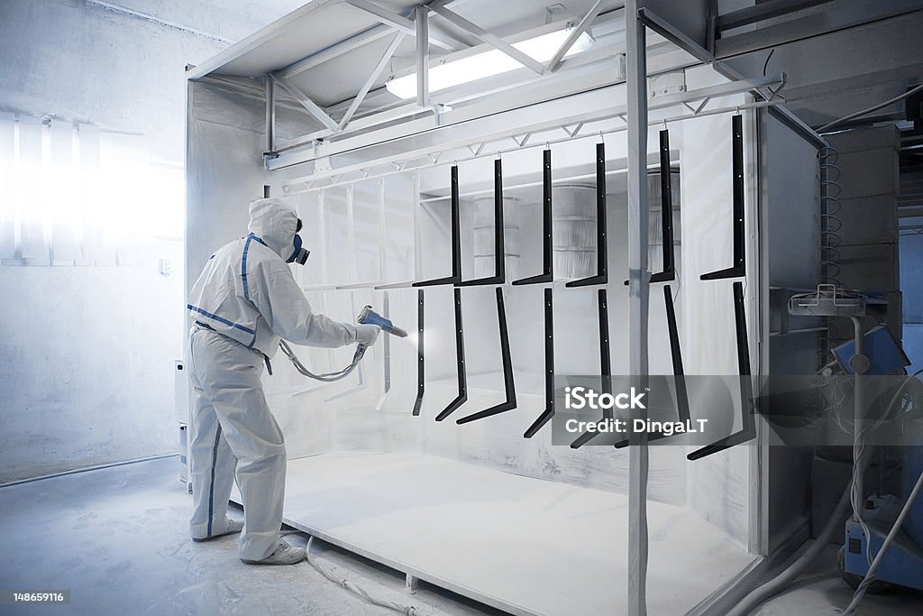 Powder coating  in a special camera Worker wearing protective wear performing powder coating of metal details in a special industrial camera Coating - Outer Layer Stock Photo