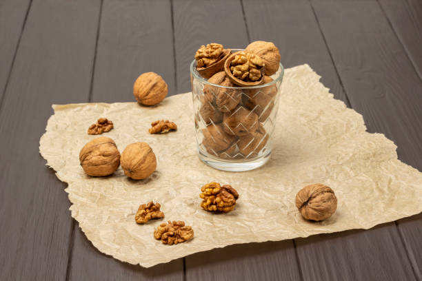 istock Whole and cracked walnuts in a glass on paper. Walnut shells and kernel on table. 1486593250
