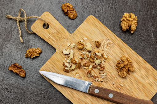 Crushed walnuts and knife on cutting board. Walnut shell and walnut kernels on the table. Flat lay. Brown background.