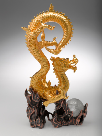 An ornate Gold Plated Dragon figurine with a quartz orb, a symbol of tenacity and entrepreneurial spirit. Isolated on gradual grey tone background.