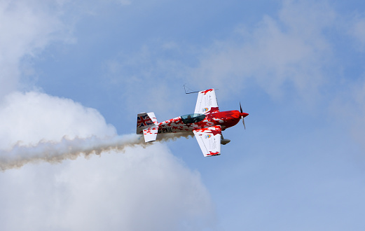 Little Gransden, Cambrigeshire, England - August 28, 2022:   Global All Stars Extra 300S stunt aircraft in flight with smoke
