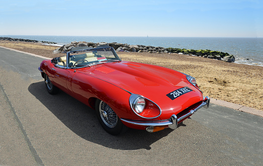 Felixstowe, Suffolk, England -  May 01, 2016: Classic  Red E-Type Jaguar Car parked on seafront promenade beach and sea in background.