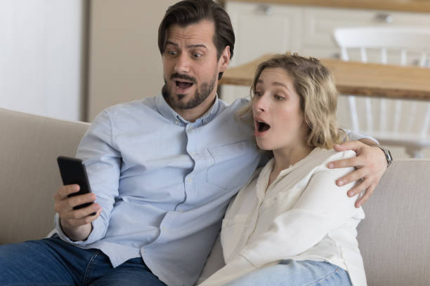 un jeune couple choqué et confus reçoit des nouvelles surprenantes inattendues - women computer couple surprise photos et images de collection