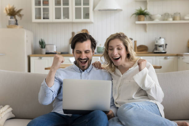 Happy excited young couple holding laptop, shouting for joy stock photo