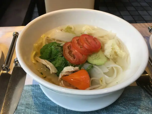 Comforting bowl of hot asian inspired chicken noodle soup with fresh tomatoes and cucumbers in Vietnam.