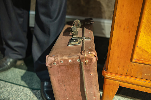 A very old suitcase stands next to a person's foot