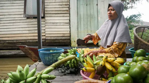 Photo of Banjar women at the house by the river are arranging fruits into baskets