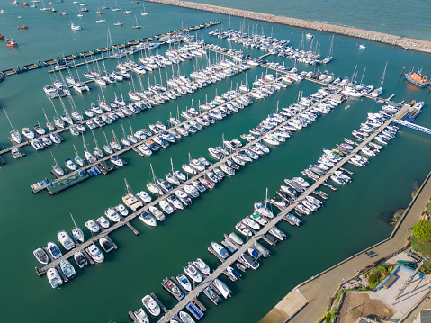 Aerial drone view of small yachts & boats moored in a the popular Devon marina of Brixham. The floating pontoons and walkways enable numerous vessels to moor safely in the harbour area, providing the opportunity for sailors to come ashore.