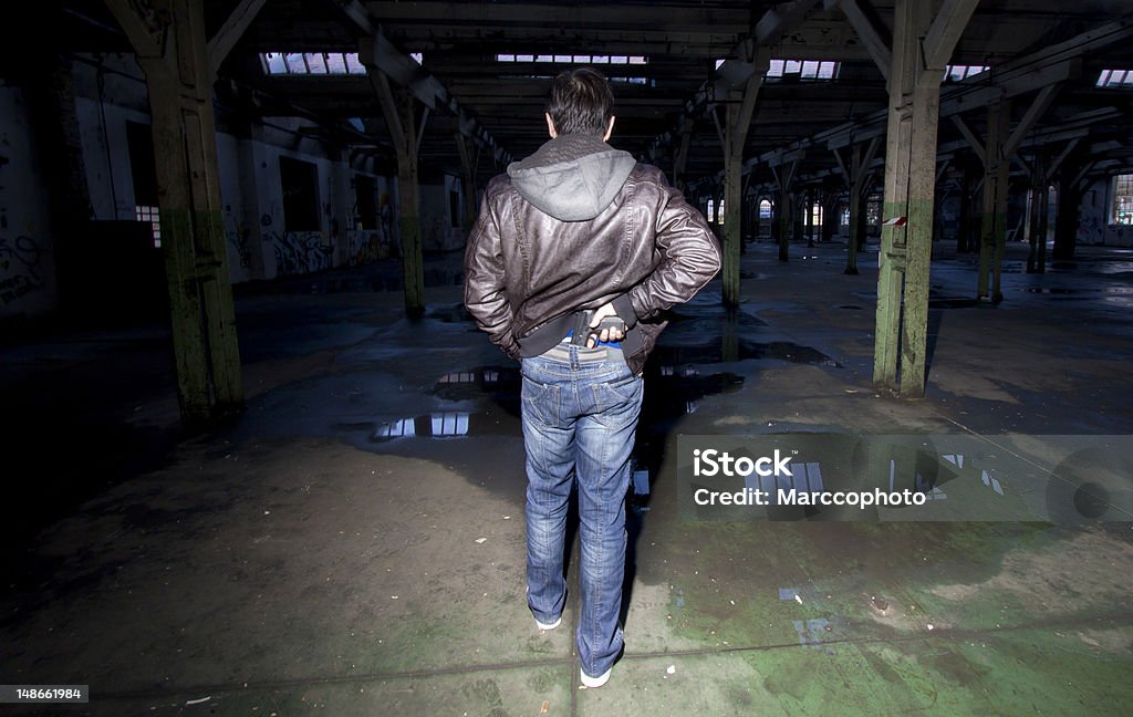 Man pulling gun from secret place on his waist Man pulling gun from secret place on his waist. Rear, follow view. Photo is taken with dslr camera in dark,spooky,abandoned factory. Gun Stock Photo