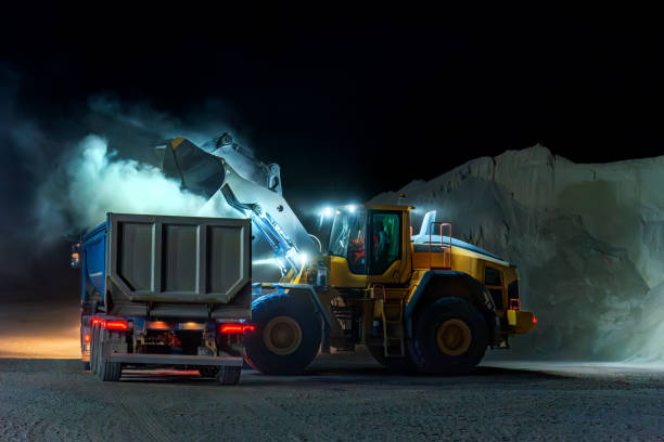Heavy construction and mining machinery loading a dump truck with gravel in a quarry on the night shift.