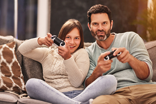 Father, child and playing games in home living room, having fun and bonding on sofa. Dad, gaming and happy teenager, girl and gamer daughter on esports, video game and enjoying time together at night