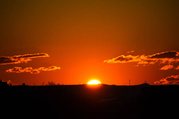 Sun hiding behind the mountains, with windmills on the sides and small clouds.