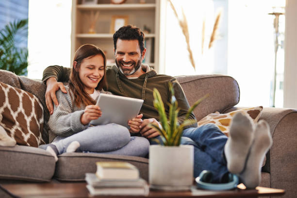 Tablet, happy man and teenager girl on sofa checking social media meme and quality time to relax in home. Lounge, dad and daughter on couch, internet post and laughing together, bonding and happiness stock photo