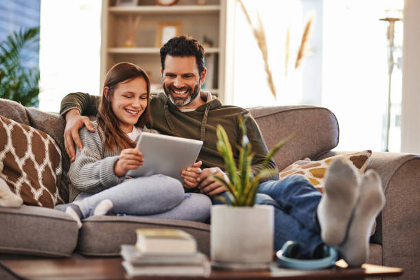 tablet, homem feliz e menina adolescente no sofá verificando meme de mídia social e tempo de qualidade para relaxar em casa. lounge, pai e filha no sofá, post na internet e rindo juntos, união e felicidade - digital tablet family father offspring - fotografias e filmes do acervo