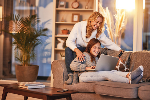 Laptop, credit card and couch, mother and daughter shopping online, quality time and relax in home. Smile, teenager girl and happy woman on sofa together, ecommerse and evening bonding in happiness.