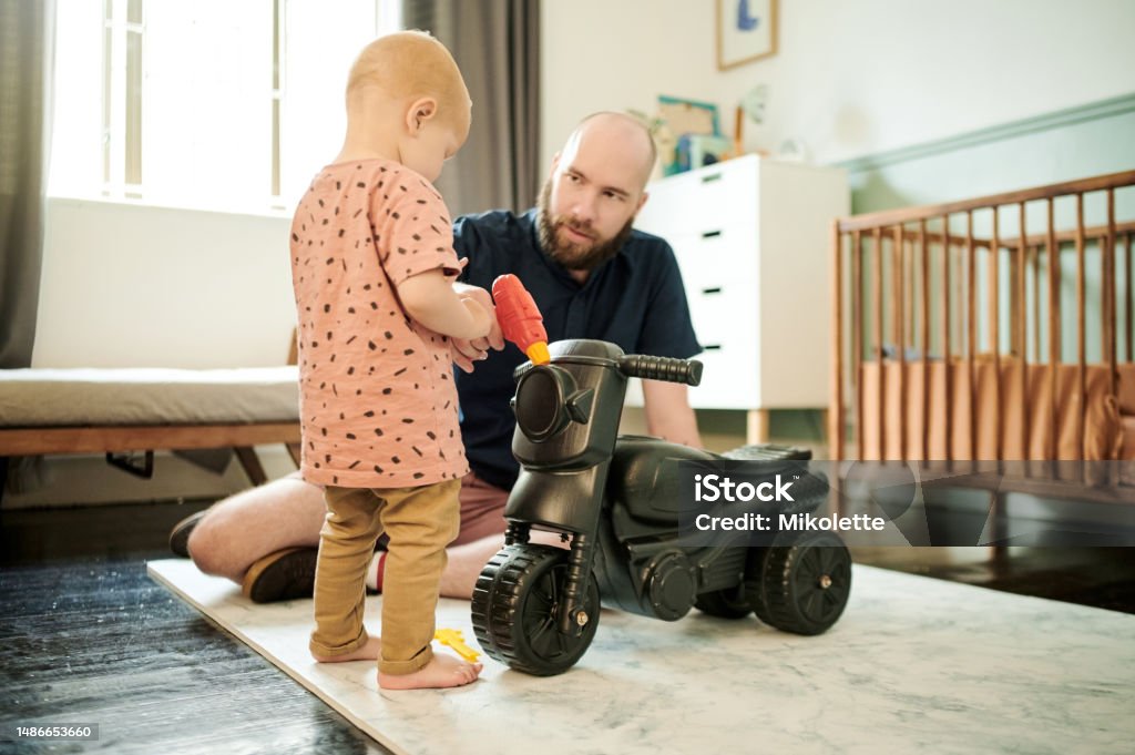 Dad, baby and living room walking for motor skills, learning and growth in a home. House, family and young kid with father playing with toy car with love, parent support and care for toddler 18-23 Months Stock Photo