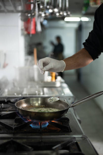 A male chef preparing food over a flaming gas stove with pan in restaurant kitchen.