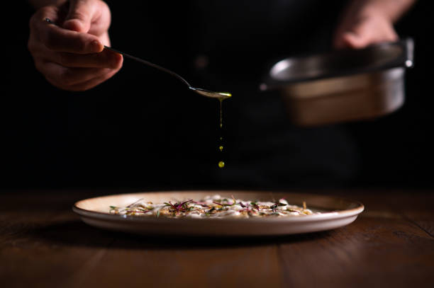 A male chef pouring sauce on a plate of carpaccio A male chef pouring sauce on a plate of carpaccio. carpaccio parmesan cheese beef raw stock pictures, royalty-free photos & images