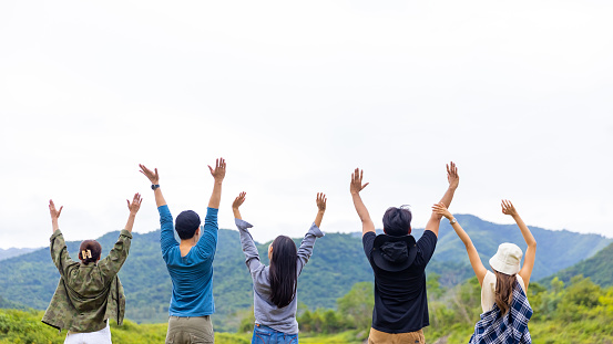 Group of Asian people enjoy and fun outdoor lifestyle hiking and camping together in nature on summer travel vacation. Man and woman friends standing by the lake with raise hand up with happiness.