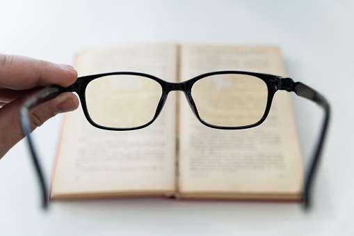 book and eye glasses for read and write over blurred background with copy space, selective focus. reading glasses in his hands on a blurry book background. poor vision concept. loss of vision,